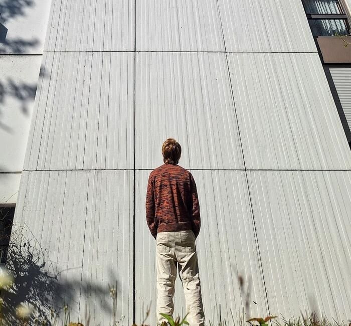 The author standing over a grass field, looking slightly above at a wall texturized with vertical stripes